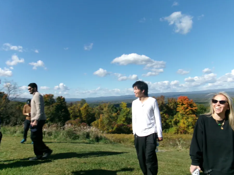 Teammates laughing on a hilltop meadow above autumn foliage